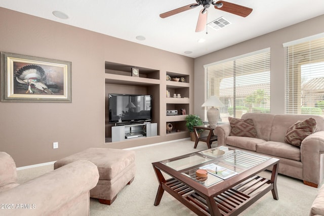 living room with built in shelves, baseboards, visible vents, ceiling fan, and light colored carpet