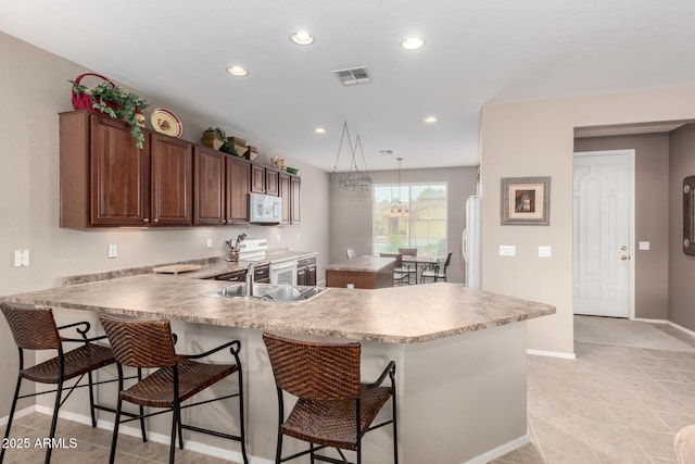 kitchen featuring visible vents, a kitchen island, light countertops, white appliances, and a sink