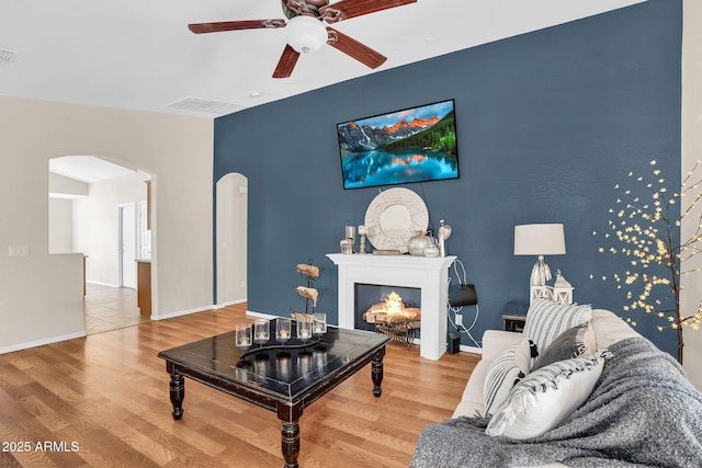 2738 E Silversmith Trl, San Tan Valley, AZ 85143 - living room with arched walkways, a ceiling fan, wood finished floors, a lit fireplace, and baseboards