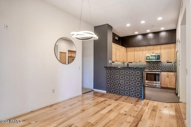 kitchen with appliances with stainless steel finishes, hanging light fixtures, light hardwood / wood-style floors, decorative backsplash, and a chandelier