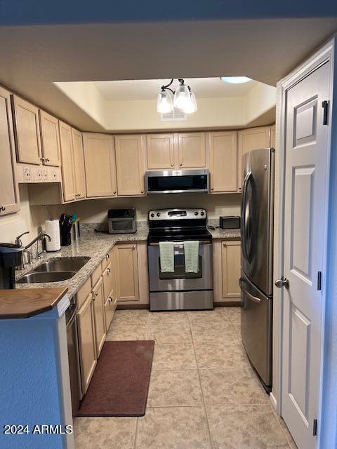 kitchen featuring appliances with stainless steel finishes, sink, light brown cabinetry, light tile patterned floors, and a chandelier