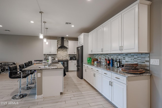 kitchen with pendant lighting, white cabinets, fridge, light stone countertops, and wall chimney exhaust hood