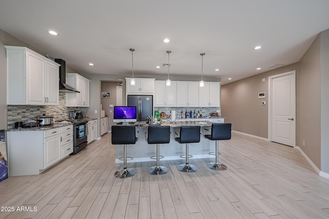 kitchen featuring stainless steel fridge, white cabinets, a center island with sink, black range oven, and decorative light fixtures