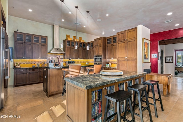 kitchen with a center island with sink, a kitchen breakfast bar, wall chimney range hood, and light tile patterned flooring