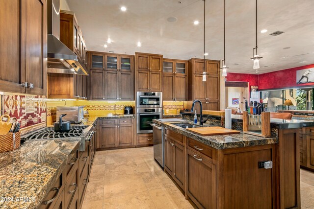 kitchen with light tile patterned floors, an island with sink, sink, decorative backsplash, and wall chimney exhaust hood