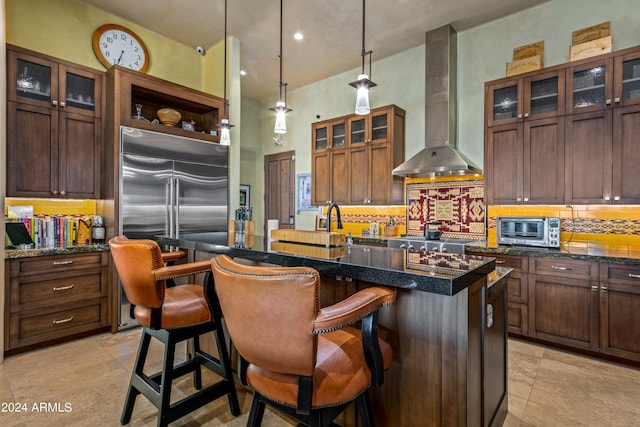 kitchen with dark stone counters, light tile patterned floors, decorative backsplash, a center island with sink, and wall chimney range hood