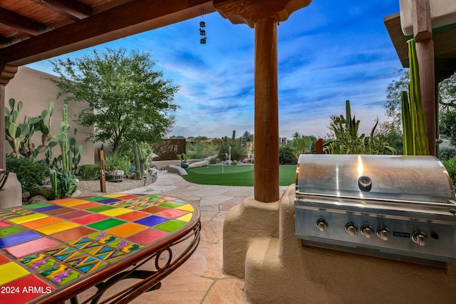 patio terrace at dusk featuring a grill and an outdoor kitchen