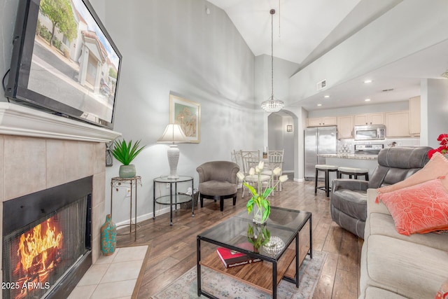 living room featuring high vaulted ceiling, wood-type flooring, a tile fireplace, and an inviting chandelier