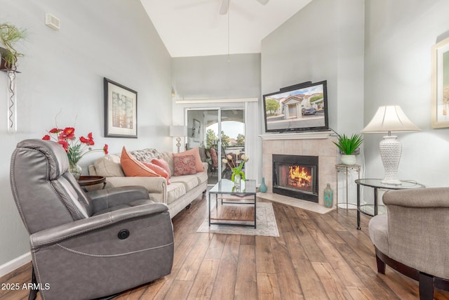 living room with wood-type flooring, high vaulted ceiling, ceiling fan, and a tiled fireplace