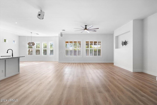 unfurnished living room with light wood-type flooring, ceiling fan, and sink