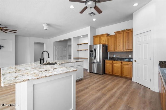 kitchen with stainless steel fridge, sink, an island with sink, and light wood-type flooring