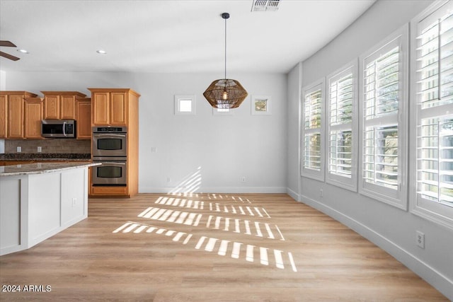 kitchen with a wealth of natural light, light hardwood / wood-style floors, backsplash, and appliances with stainless steel finishes