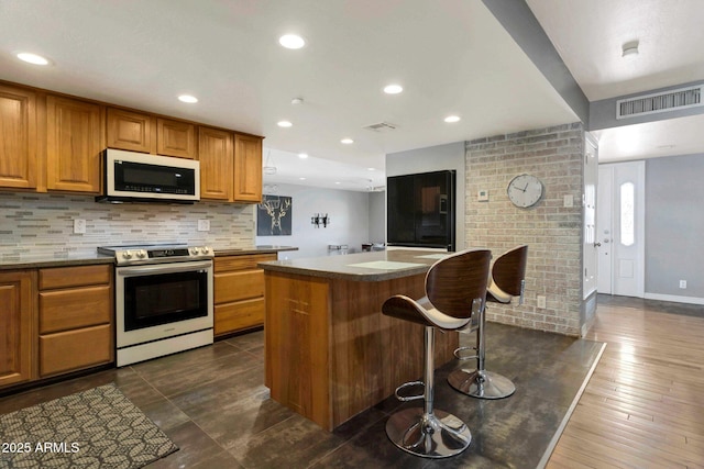 4304 W Calle Poco, Laveen, AZ 85339 - kitchen featuring stainless steel range with electric stovetop, white microwave, brown cabinets, a kitchen island, and tasteful backsplash