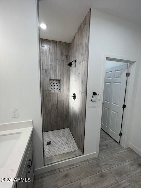 bathroom featuring tile patterned flooring, a tile shower, and vanity