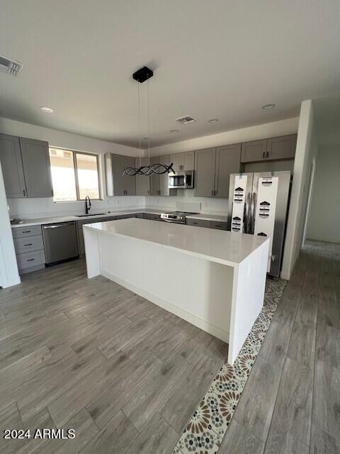 kitchen with appliances with stainless steel finishes, hardwood / wood-style floors, sink, a kitchen island, and gray cabinets