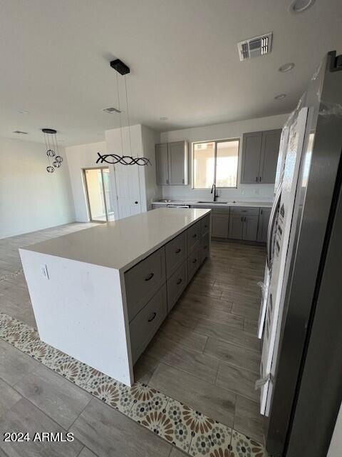 kitchen featuring stainless steel refrigerator, sink, gray cabinetry, a kitchen island, and hanging light fixtures