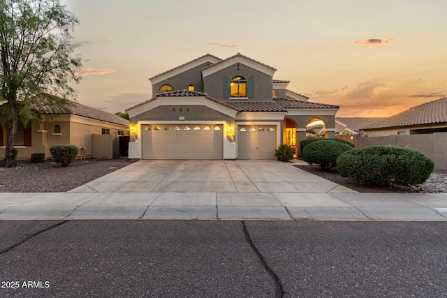 mediterranean / spanish house with a tiled roof, driveway, fence, an attached garage, and stucco siding