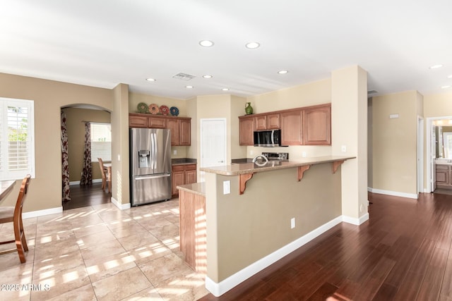 kitchen featuring visible vents, a peninsula, a breakfast bar, arched walkways, and stainless steel appliances