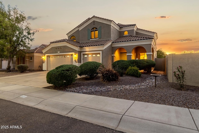 mediterranean / spanish-style house with fence, stucco siding, concrete driveway, and a tile roof