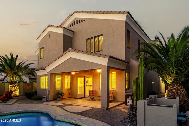 rear view of property with a tiled roof, french doors, fence private yard, a patio, and stucco siding