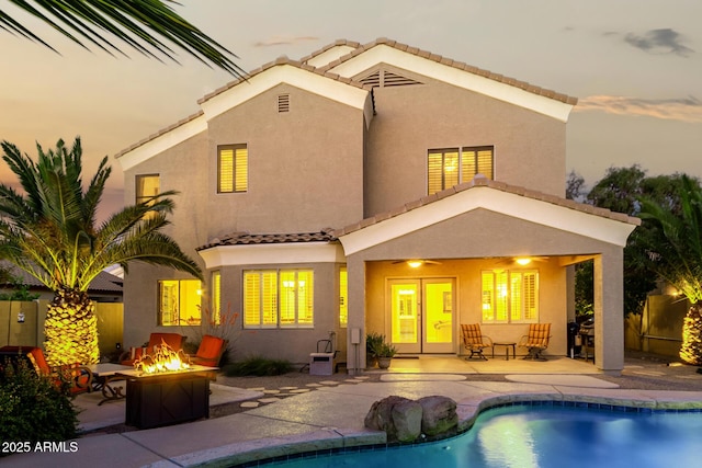 back of house with an outdoor fire pit, a tile roof, stucco siding, an outdoor pool, and a patio