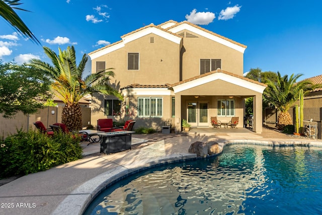 rear view of house featuring a fenced in pool, stucco siding, a fire pit, and a patio area