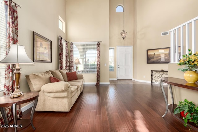 living room with a high ceiling, visible vents, a healthy amount of sunlight, and dark wood-type flooring