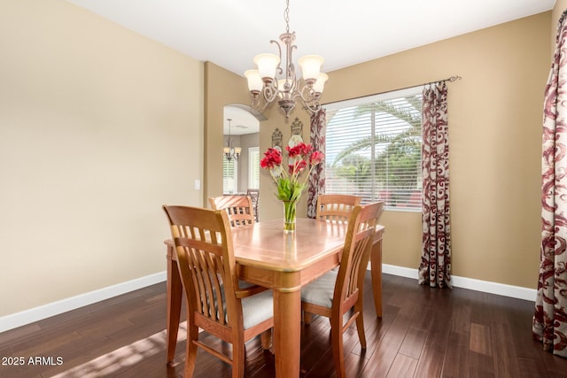 dining space with an inviting chandelier, baseboards, arched walkways, and dark wood-type flooring