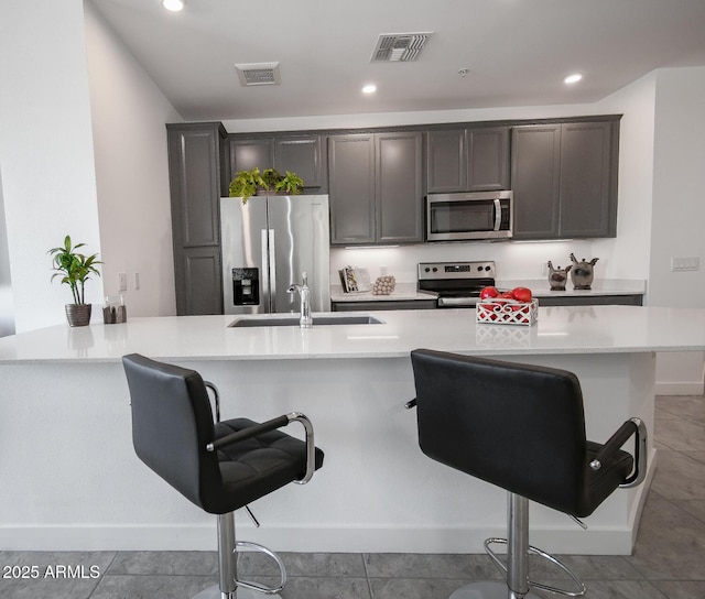 kitchen with appliances with stainless steel finishes, a kitchen island with sink, light tile patterned flooring, a breakfast bar, and sink