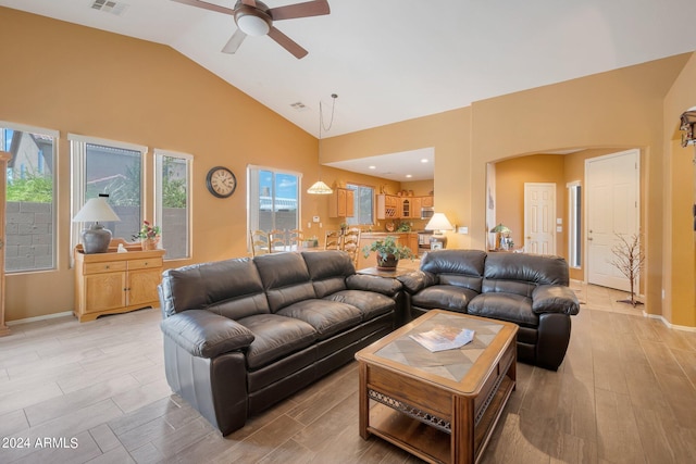 living area featuring arched walkways, high vaulted ceiling, light wood-style floors, and a healthy amount of sunlight