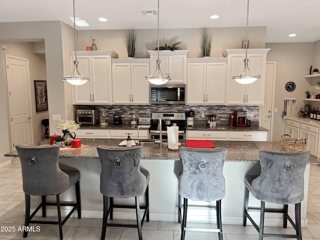 kitchen featuring a breakfast bar, pendant lighting, tasteful backsplash, a kitchen island with sink, and stainless steel appliances