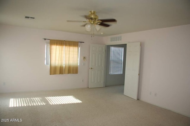 carpeted empty room featuring visible vents and a ceiling fan