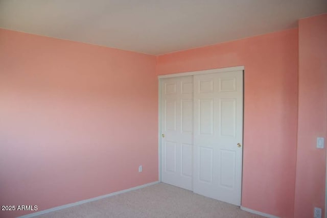 unfurnished bedroom featuring light carpet, baseboards, and a closet