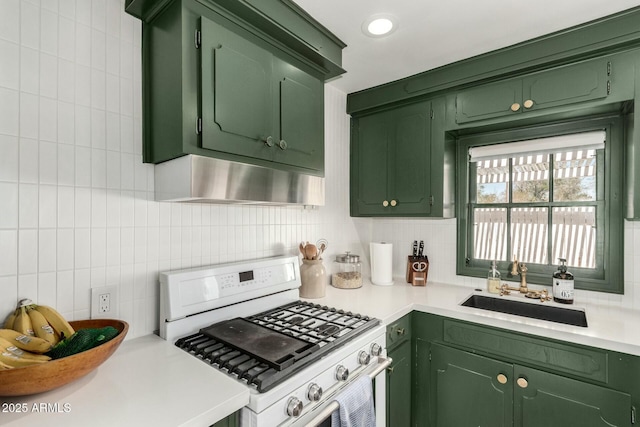 kitchen with white range with gas stovetop, light countertops, wall chimney range hood, green cabinets, and a sink