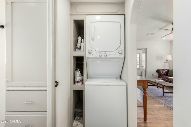 clothes washing area with stacked washer and dryer, laundry area, light wood finished floors, visible vents, and a ceiling fan