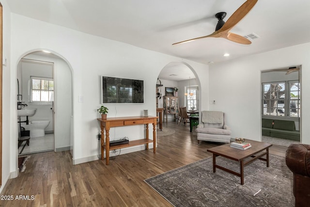 living room featuring arched walkways, visible vents, ceiling fan, wood finished floors, and baseboards