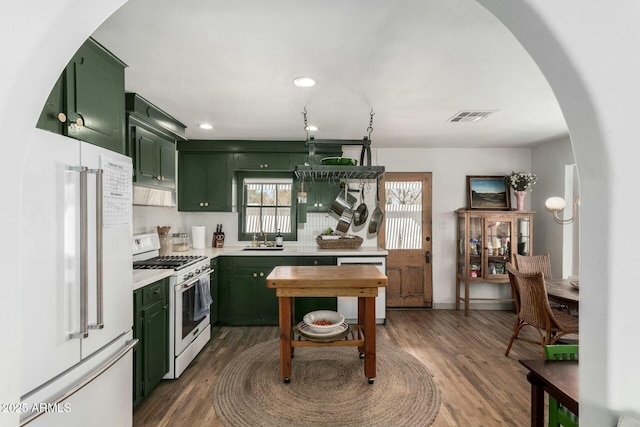 kitchen with white appliances, arched walkways, green cabinets, and light countertops