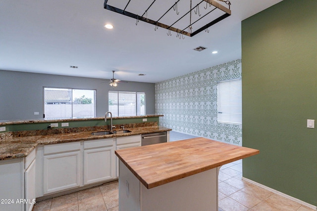 kitchen with stainless steel dishwasher, wooden counters, a sink, white cabinetry, and a ceiling fan
