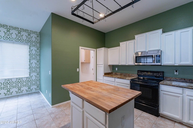 kitchen featuring black range with electric stovetop, light tile patterned floors, a kitchen island, white cabinetry, and dark stone counters