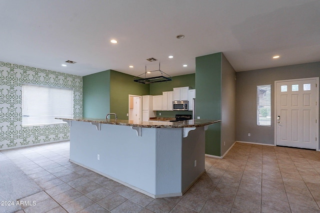 kitchen with dark stone countertops, stainless steel microwave, a breakfast bar, wallpapered walls, and white cabinets
