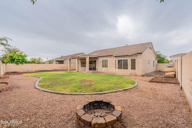 rear view of property featuring an outdoor fire pit, a fenced backyard, stucco siding, a yard, and a tiled roof