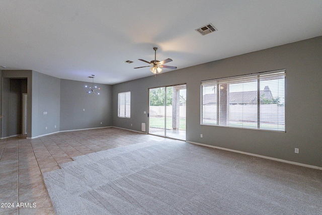 spare room featuring light carpet, ceiling fan with notable chandelier, and a healthy amount of sunlight