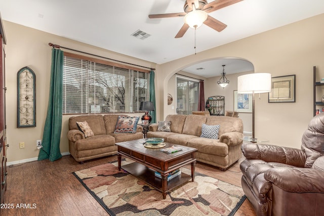 living area with arched walkways, visible vents, ceiling fan, wood finished floors, and baseboards