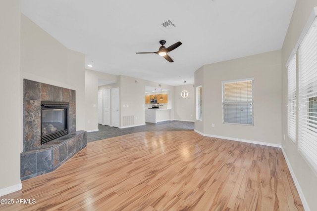 20121 N 76th St Unit 2021, Scottsdale, AZ 85255 - unfurnished living room featuring wood finished floors, a tile fireplace, a ceiling fan, and baseboards