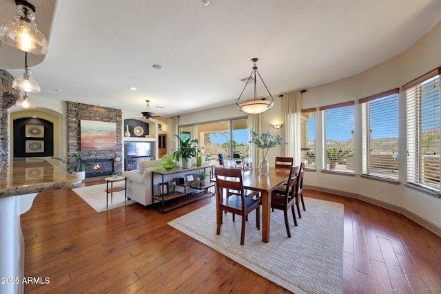 dining area featuring baseboards, hardwood / wood-style floors, and a stone fireplace