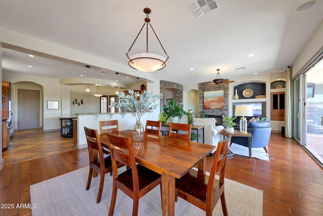 dining area with arched walkways, built in shelves, a fireplace, visible vents, and hardwood / wood-style floors