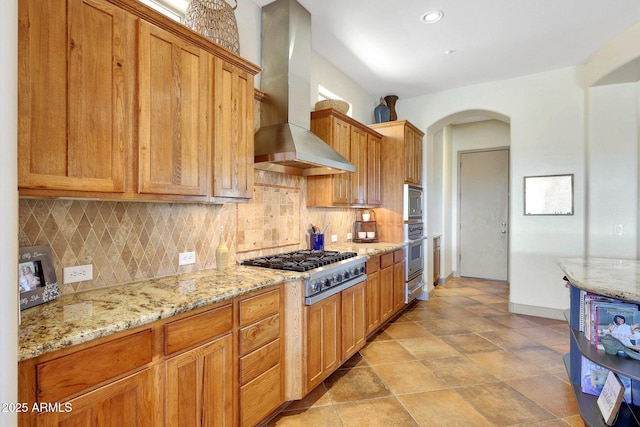 kitchen featuring backsplash, island range hood, stainless steel appliances, and arched walkways