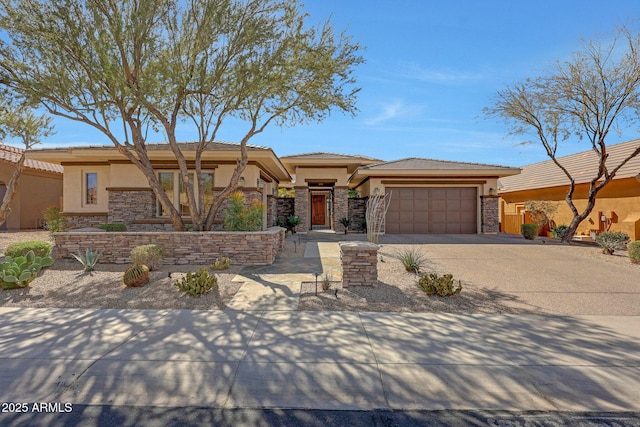 prairie-style home with a garage, stone siding, concrete driveway, and stucco siding