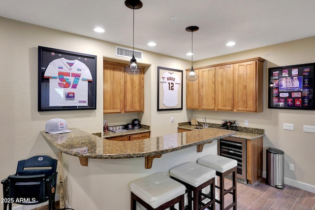 kitchen with visible vents, dark stone counters, a breakfast bar, a peninsula, and a sink