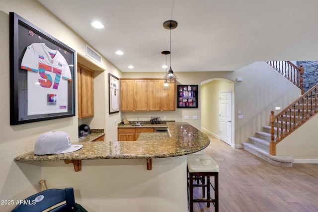 kitchen featuring stone countertops, visible vents, arched walkways, a kitchen breakfast bar, and wood finished floors